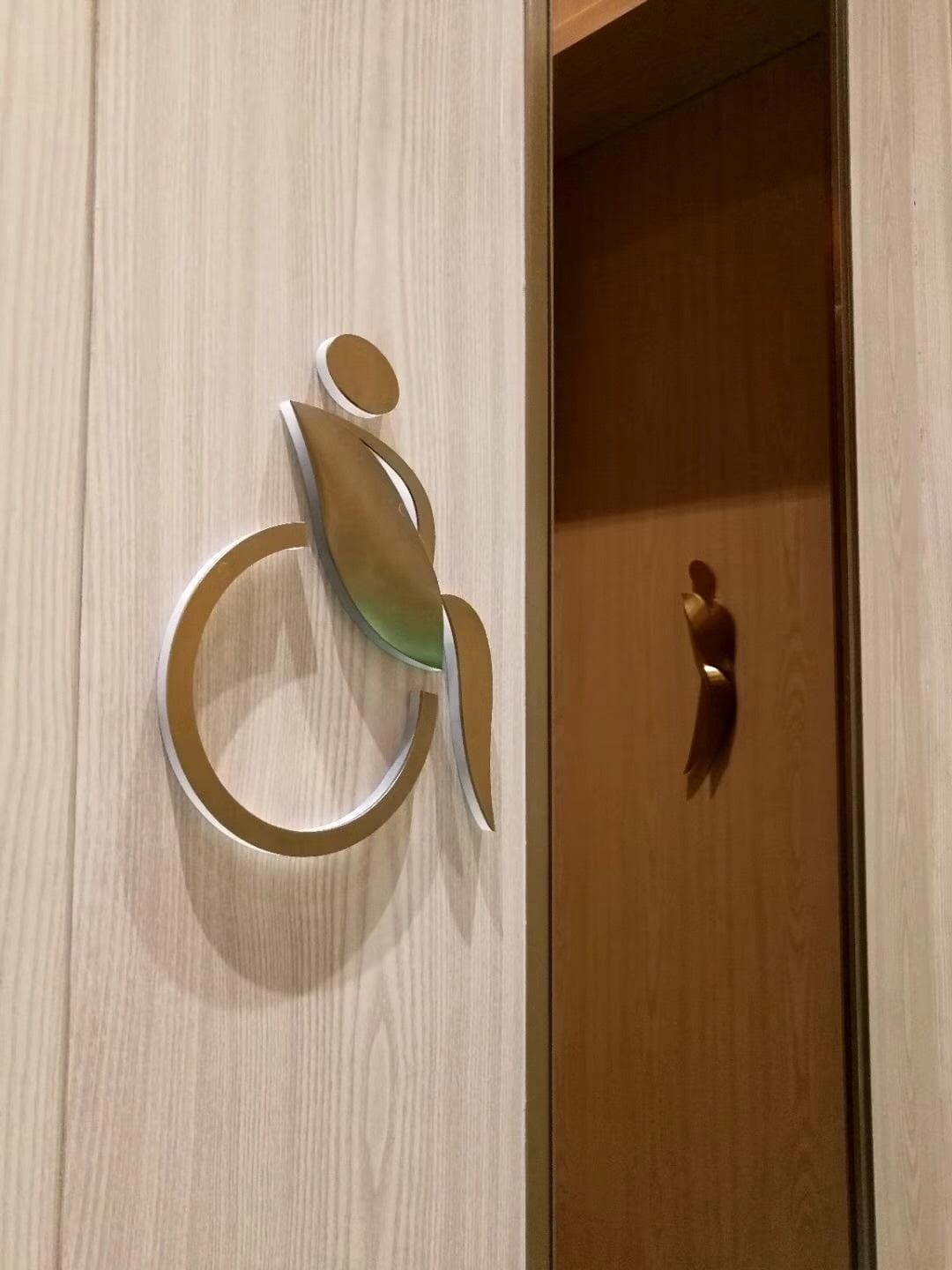3D accessibility pictogram in brushed steel mounted on wooden wall